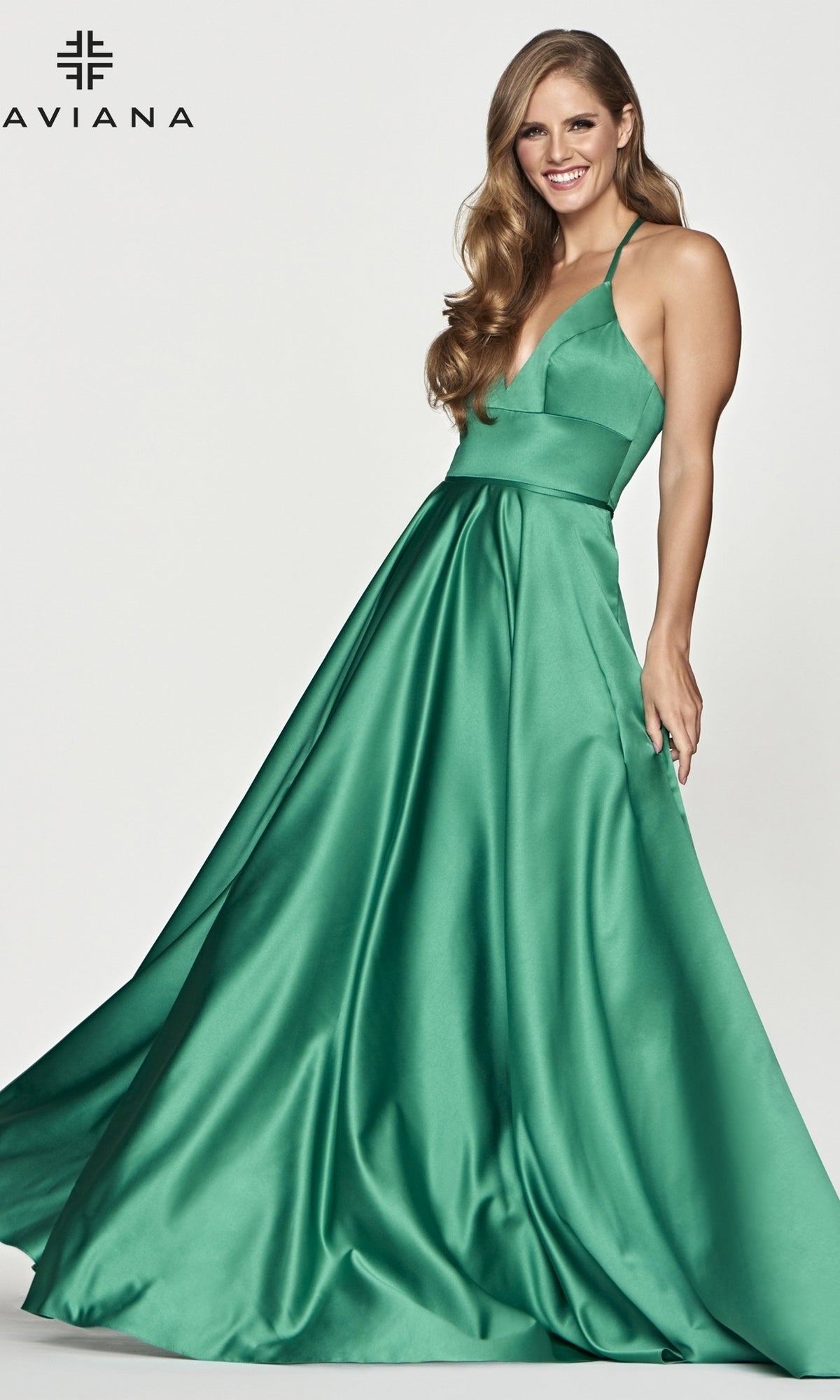 A woman stands smiling against a plain background wearing the Corset-Back A-Line Long Satin Prom Dress by Faviana, featuring a sleeveless fitted bodice, flared floor-length skirt, and striking emerald green satin fabric.